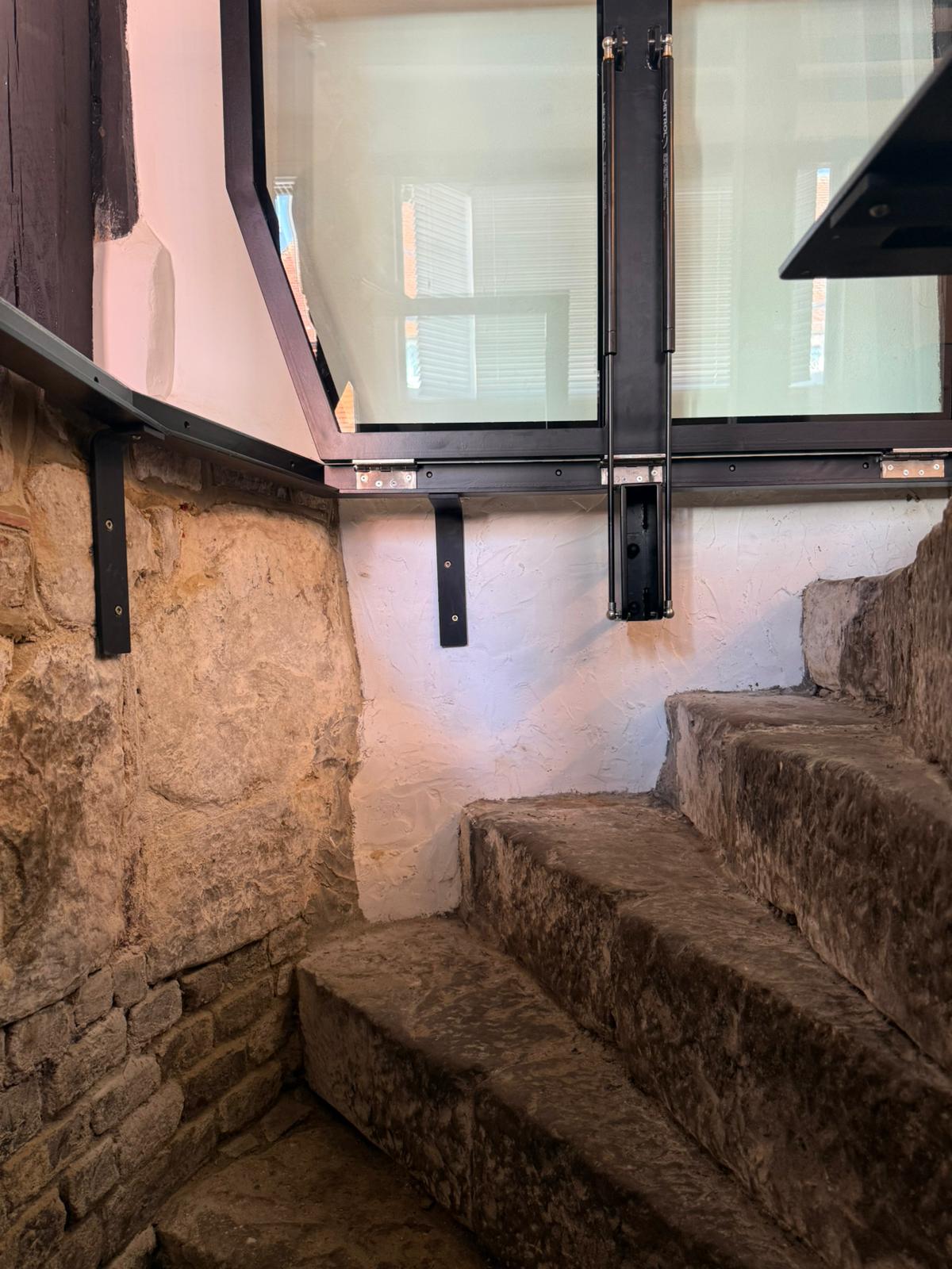 View from below showing powder coated steel brackets and gas struts supporting hinged glass floor, ancient stone staircase, Burwash